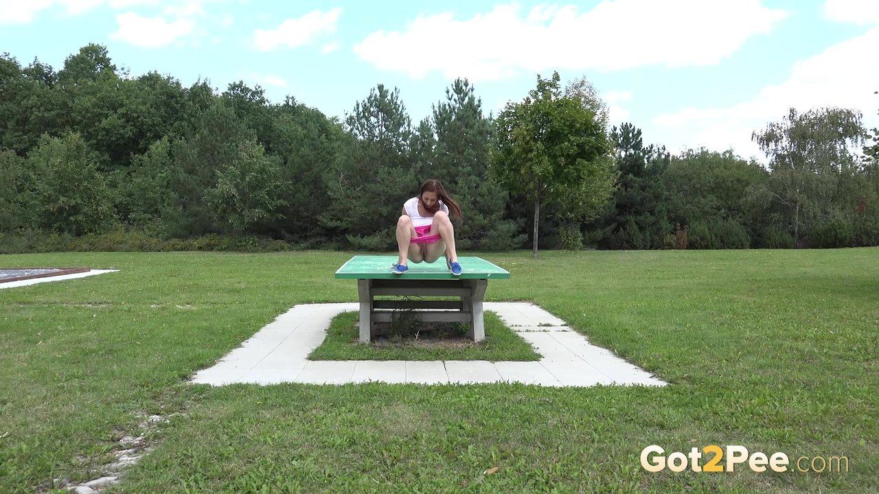 Откровенная молодая девушка в розовых шортах писает в парке