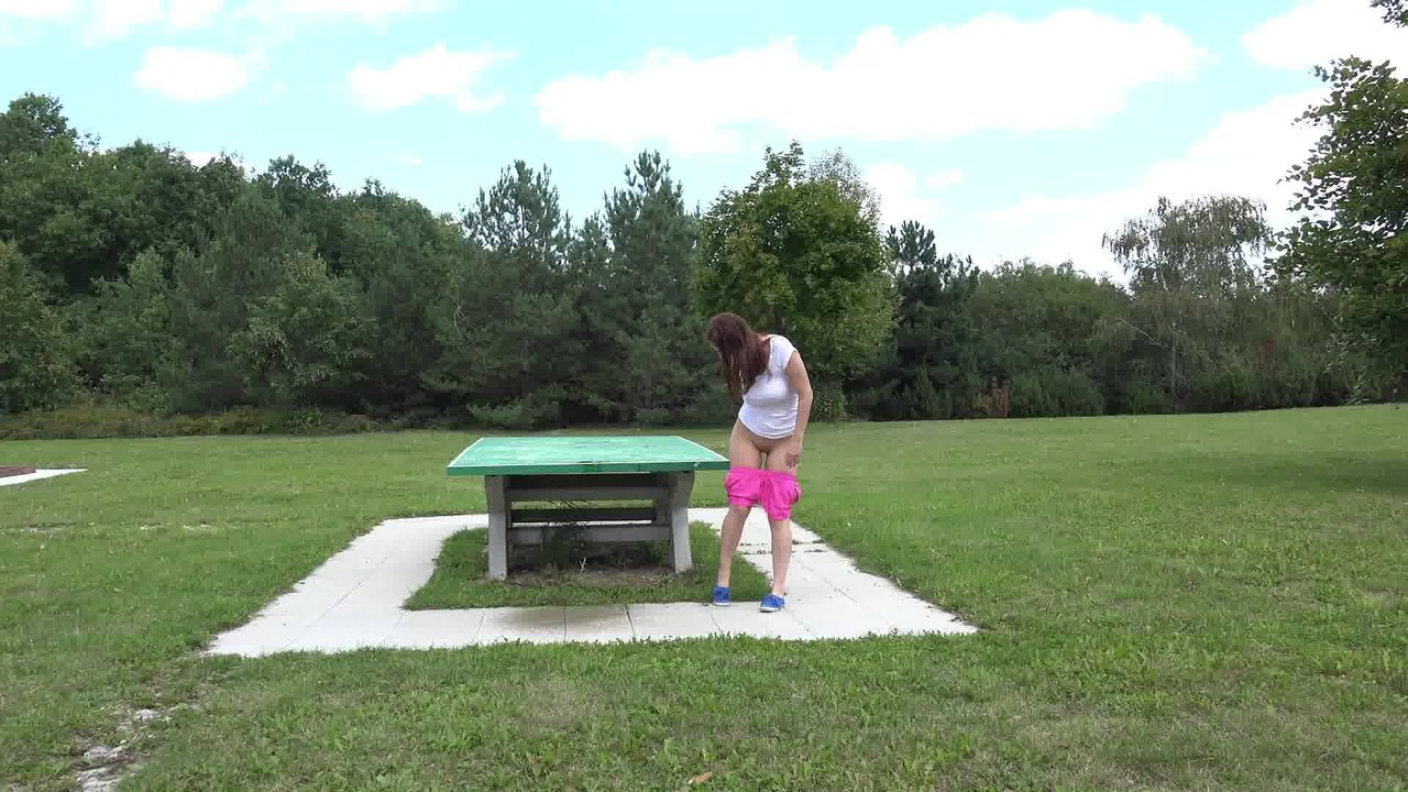 Откровенная молодая девушка в розовых шортах писает в парке