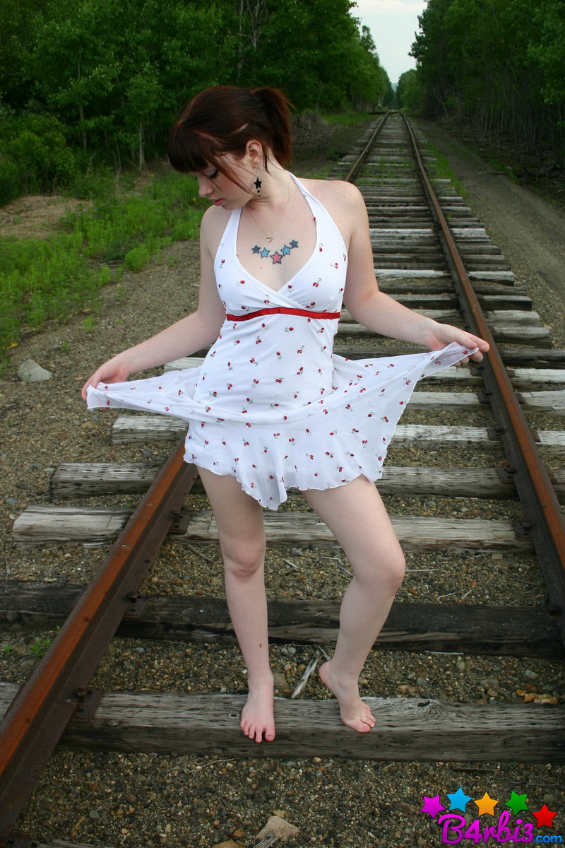 Девушка в белом сарафане фотографируется на железнодорожных путях